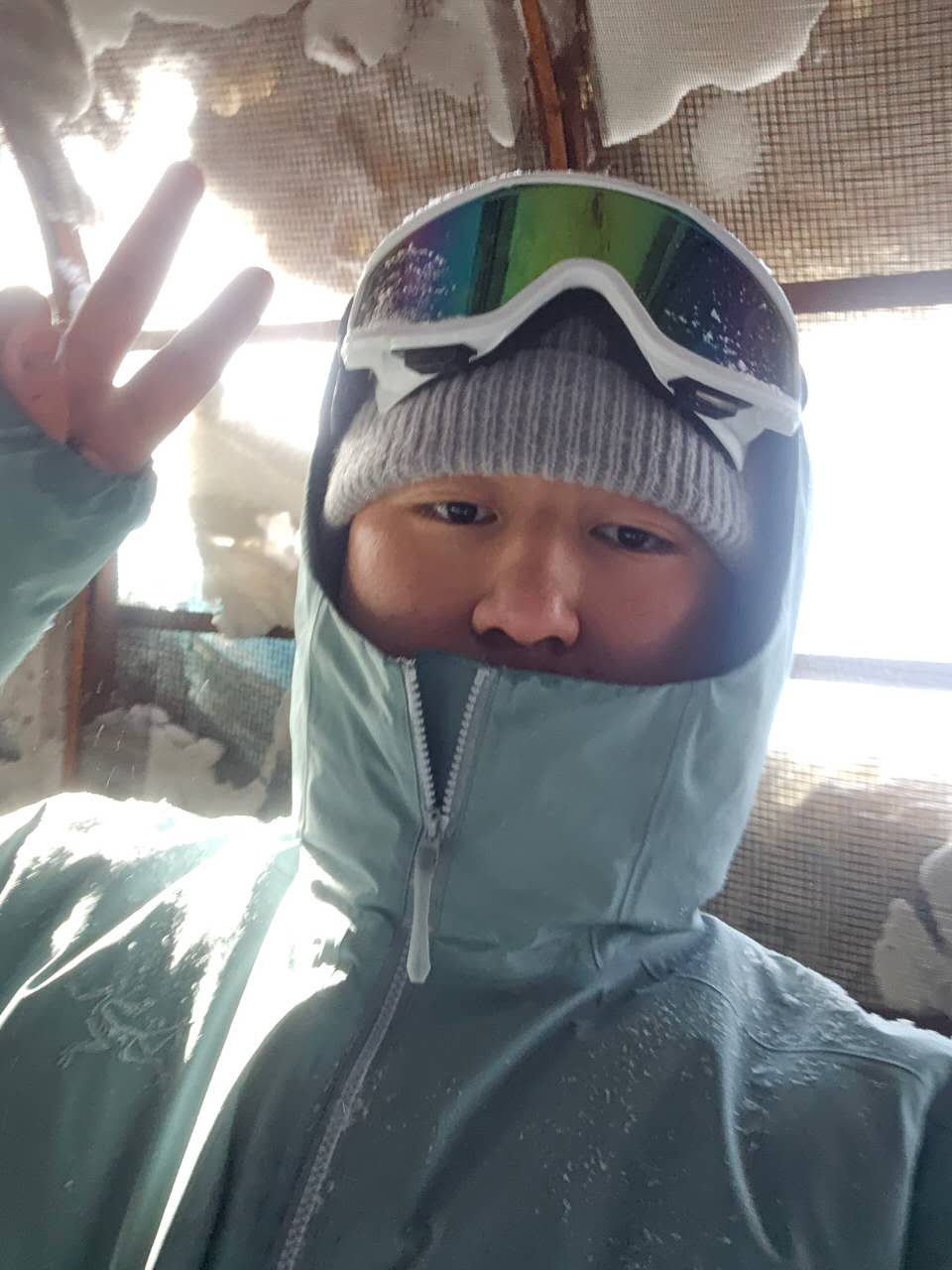 Pengyu Feng wearing ski goggles and winter gear, making a peace sign